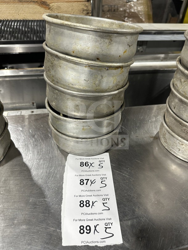Commercial stainless steel deep-dish pizza pans, stacked, used condition, with auction labels for quantity and bid information.