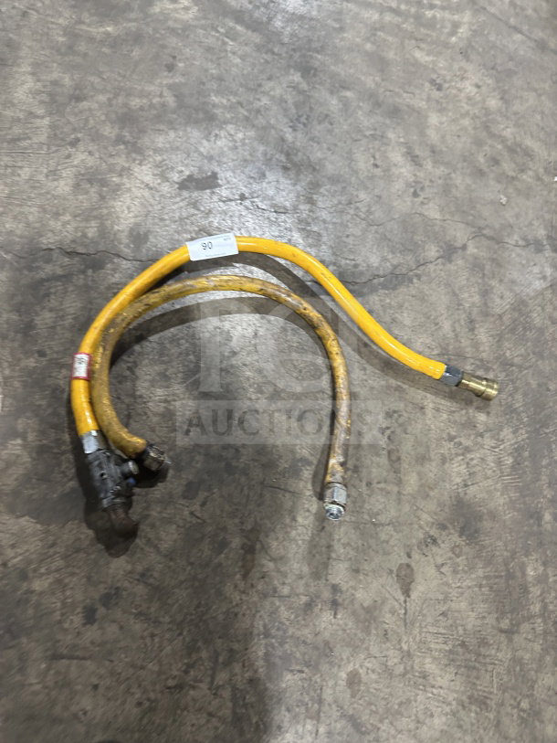 Yellow commercial gas connector hose on concrete floor, shows wear. Features metal fittings and visible tags indicating size and specifications.