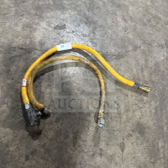 Yellow commercial gas connector hose on concrete floor, shows wear. Features metal fittings and visible tags indicating size and specifications.