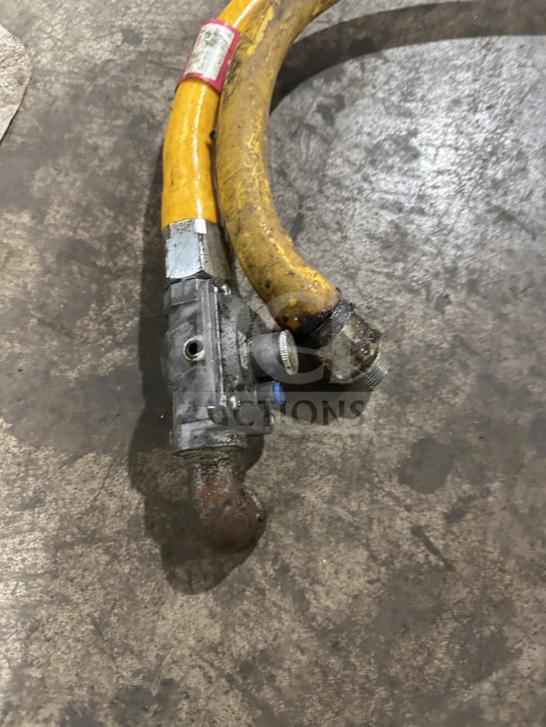 Yellow commercial gas connector hose, visible wear, metal fittings, attached valve, safety label present.