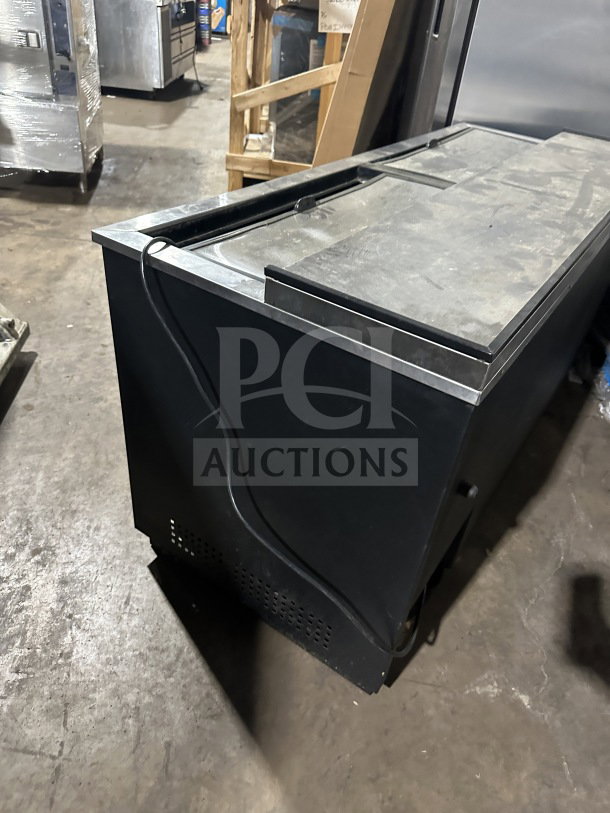 True commercial black horizontal forced air bottle cooler with stainless steel worktop and dual easy-slide access lid, used condition.