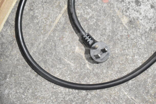 Black power cord with three-prong plug lying on a textured, gray concrete surface.