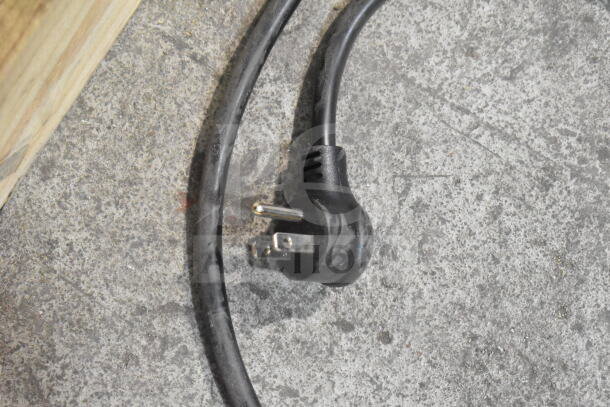 Black power cord with three-prong plug on textured ground, part of True TVM-48SL-HC cooler.