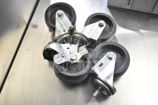 Lot of 4 commercial casters, metal with rubber wheels, slightly used, sturdy design, includes mounting hardware.