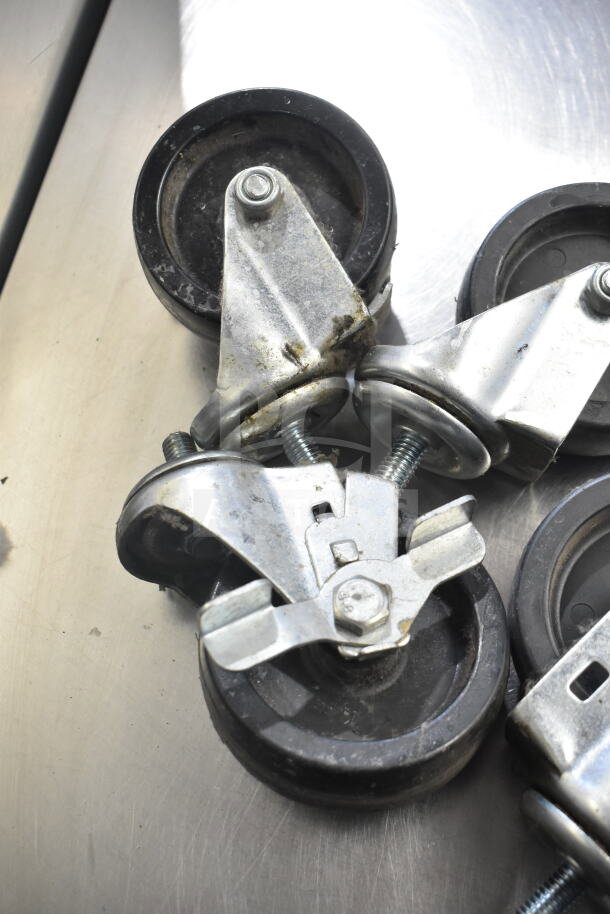 Lot of 4 commercial casters with metal brackets and black wheels, showing signs of wear.