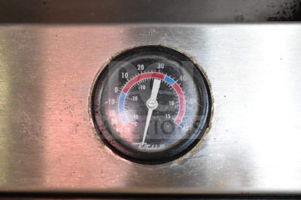 Thermometer gauge on True T-23 cooler, showing temperature range. Scratches and slight wear visible on metal surface.