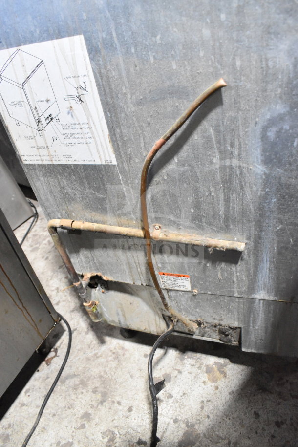 Manitowoc QD0212A undercounter ice machine, showing rear panel with visible pipes and labels, in used condition.