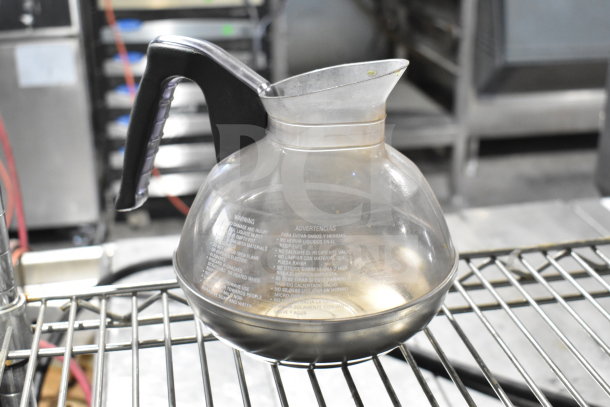 Glass coffee pot with black handle, featuring visible usage marks and safety warnings etched. Auction includes two pots.