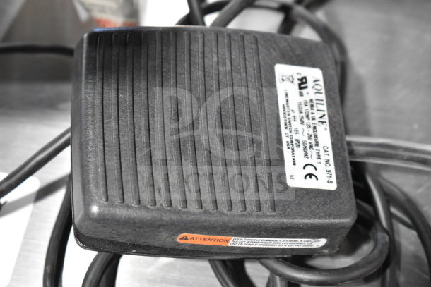 Aquiline pedal with label showing CAT No. 971-S and CE marking. Textured black surface, with attached cables.