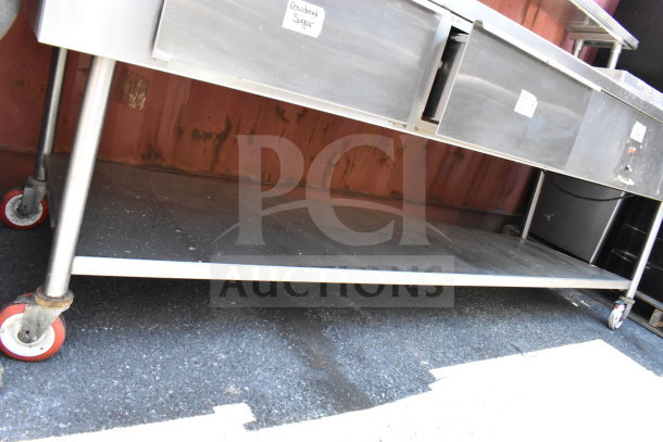 Stainless steel commercial table with 2 drawers, over shelf, under shelf, and heated well. Visible caster wheels and "Powdered Sugar" label.
