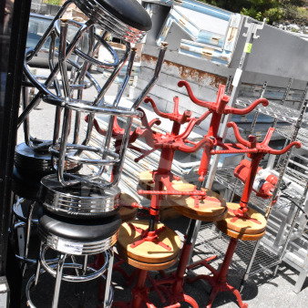 15 assorted stools in varying styles, including chrome bar stools and red industrial stools, stacked outdoors.