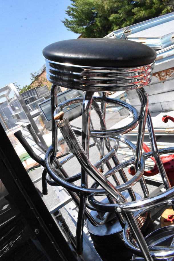 15 various chrome stools with black seats, stacked outdoors. Some minor wear visible. Auction lot for multiple bids.