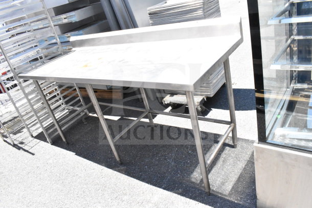 Stainless steel commercial table with backsplash, sturdy frame, visible surface wear, ideal for kitchen use.