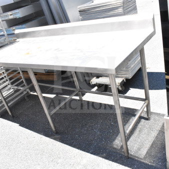 Stainless steel commercial table with backsplash, sturdy frame, visible surface wear, ideal for kitchen use.