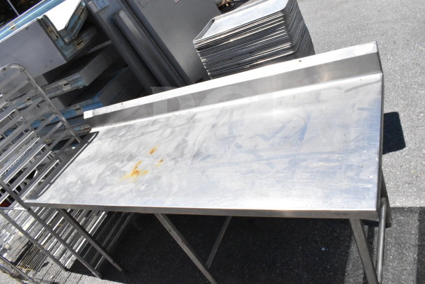 Stainless steel commercial table with a backsplash, some surface stains, sturdy metal legs, suitable for kitchen use.