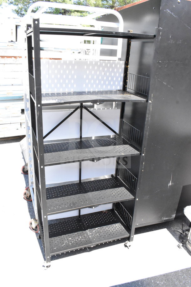 Black shelving unit with five perforated shelves on commercial casters, showing signs of light wear. Rugged construction.
