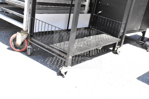Black shelving unit with perforated metal shelf and side railings, mounted on sturdy commercial casters for mobility.