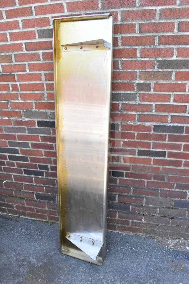 Tall metal shelf with a rectangular shape, some discoloration, and mounting holes, leaning against a brick wall.