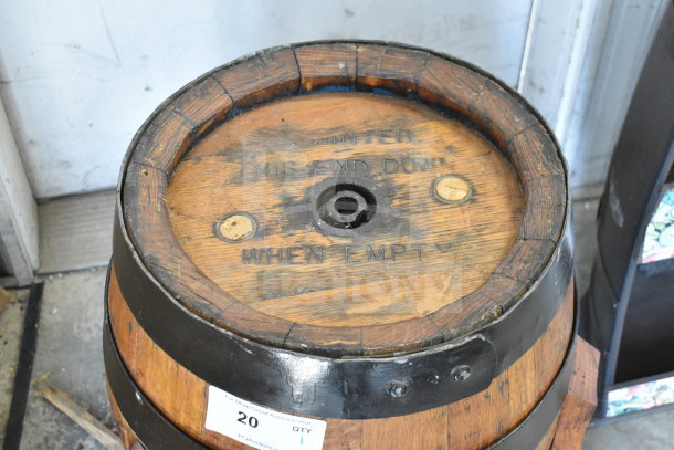 Wooden barrel with black metal bands, visible markings "THIS END DOWN WHEN EMPTY." Signs of wear, auction tag attached.