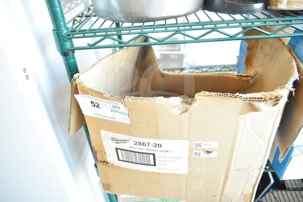 Cardboard box labeled "Milwaukee 2867-20" on a shelf, containing Oatey white latex tub-n-tile caulk tubes, visible damage to box.