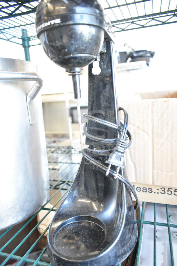 Black ST789 milkshake mixer and large aluminum stock pot on metal shelf. Mixer has cord wrapped around base. Item auction doubles bid.