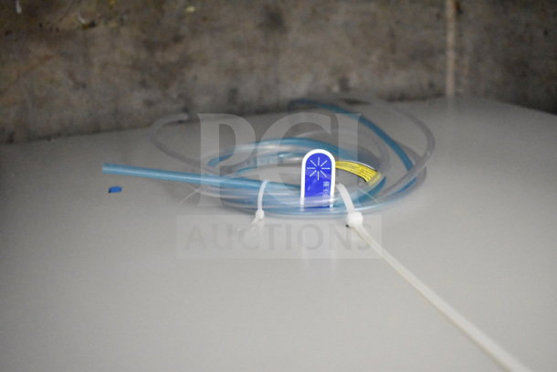 Alt text: Coiled water hose with blue label for Noble 495LTUC24 dishwasher; ties hold it in place.