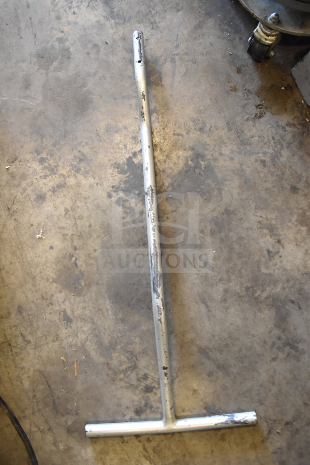 Metal bar with T-shaped ends, showing signs of wear and scratches, on a concrete surface.