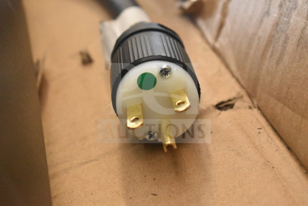 Close-up of a power plug for the Merrychef eikon e1s countertop oven, showing three prongs and a green sticker, on a cardboard surface.