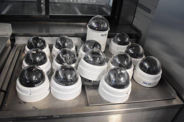 Fourteen security dome cameras with dark tinted domes, branded "Avigilon," in used condition displayed on a stainless surface.