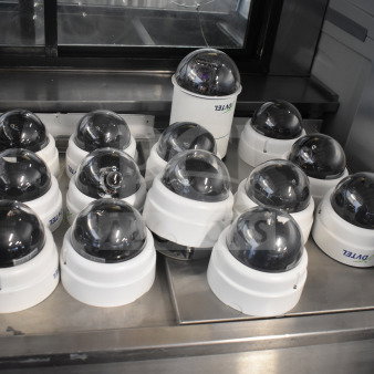 Fourteen security dome cameras with dark tinted domes, branded "Avigilon," in used condition displayed on a stainless surface.