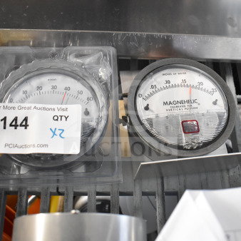 Two Magnehelic gauges, one in packaging. Measures pressure in pascals/inches of water. Auction tag reads "144 QTY 2X".