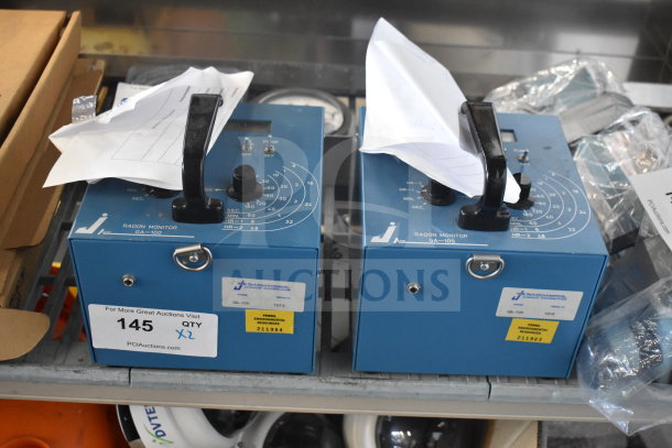 Two blue GA-100 radon monitors with handles and dials, labeled for auction.