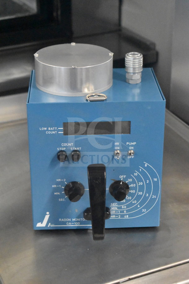 GA-100 Radon Monitor, blue, with control knobs and digital display, showing usage dials. Model GA-100 label visible.
