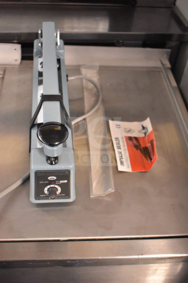 American International Electric AIE-305 Impulse Sealer, 220V, blue-gray, with instruction manual on metal surface.