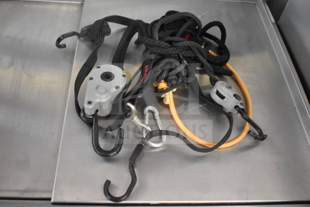 A collection of black and orange bungee cords with hooks and pulleys on a metal surface.