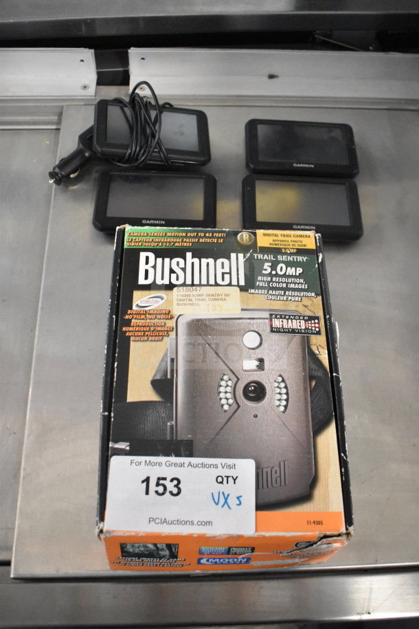 Five items including four Garmin GPS units and a Bushnell Trail Sentry 5.0 MP digital trail camera, boxed, visible auction tag.
