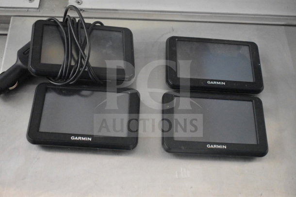 Four Garmin GPS devices and cables, alongside a Bushnell Trail Camera. Used condition, black color.