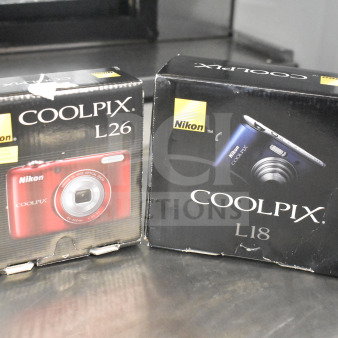 Nikon Coolpix L18 and L26 digital cameras in original boxes. Boxes show camera images and branding.