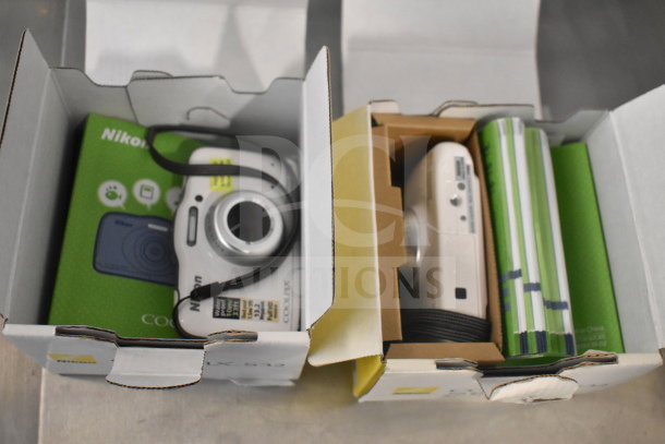 Two Coolpix S32 digital cameras in original boxes, showing labels and accessories. Cameras appear in excellent condition.