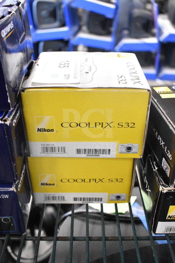 Two Nikon Coolpix S32 digital cameras in original yellow boxes, new condition, model details visible on boxes.