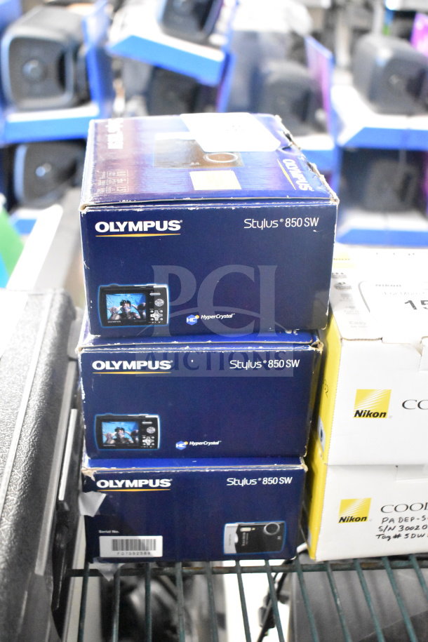 Three Olympus Stylus 850 SW digital cameras in original boxes. Boxes show brand and model info; feature HyperCrystal display.