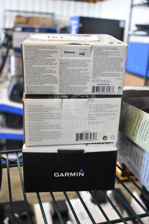 Three Garmin GPS units in original boxes: eTrex Legend H, eTrex 20, Nuvi 1390LMT. Boxes display barcodes and product details.
