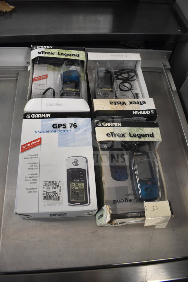 Garmin GPS units in original boxes, including GPS 76 Marine Navigator and eTrex Legend models, appear in good condition.