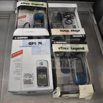 Garmin GPS units in original boxes, including GPS 76 Marine Navigator and eTrex Legend models, appear in good condition.