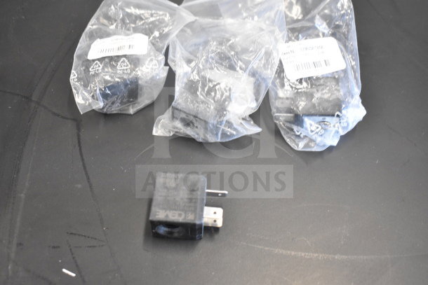 Plastic-wrapped components, possibly black relays, with visible labels. Unlabeled item in view, on a black surface.