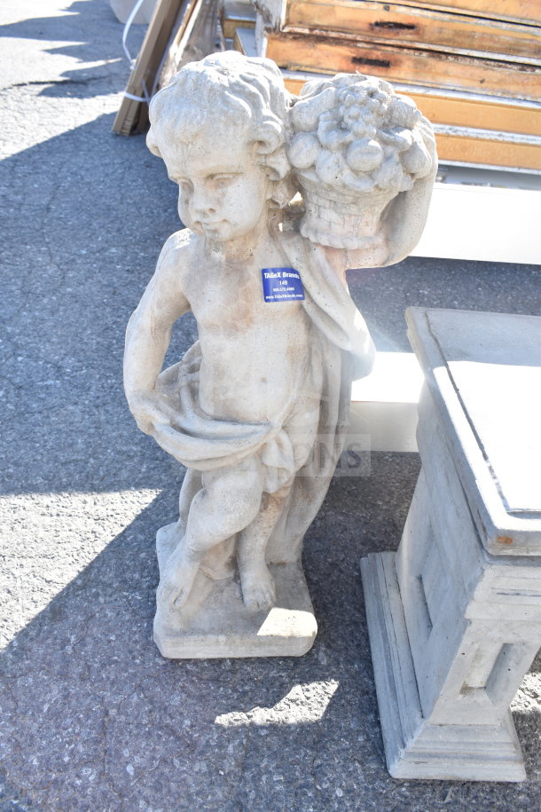 Stone statue of a cherub holding a basket, next to a concrete bench base. Visible tag includes auction information.