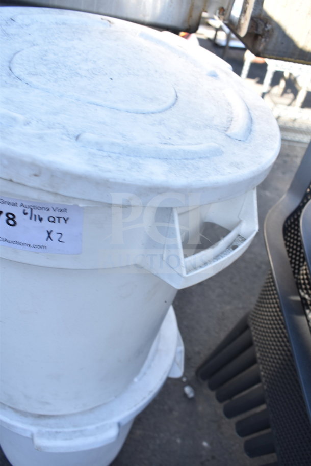 White poly trash can with lid, shows some wear. Label indicates auction lot "X2," bid for two cans.