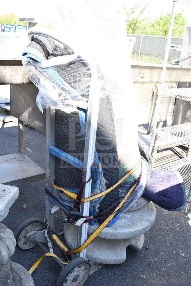 Wrapped statue secured on a dolly with protective blankets and straps, ready for transport. Condition obscured by wrapping.