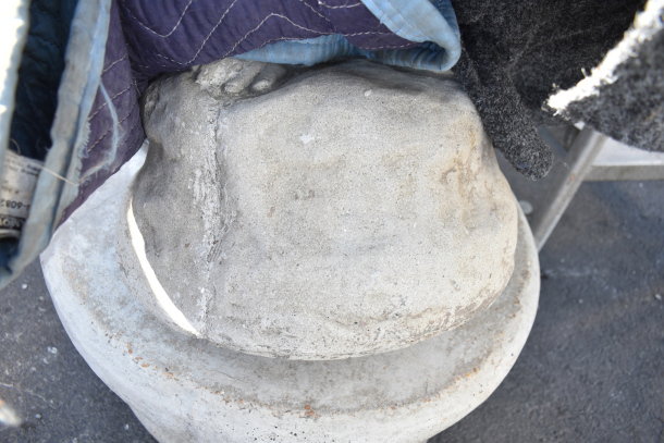 Stone statue base with visible texture, partially wrapped in dark fabric padding. Surface shows slight wear.