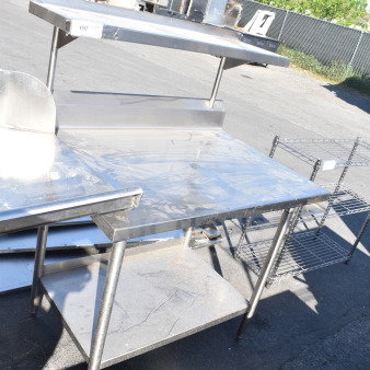 Stainless steel commercial table with over and under shelves, sturdy legs, minor scratches shown, ideal for kitchen use.